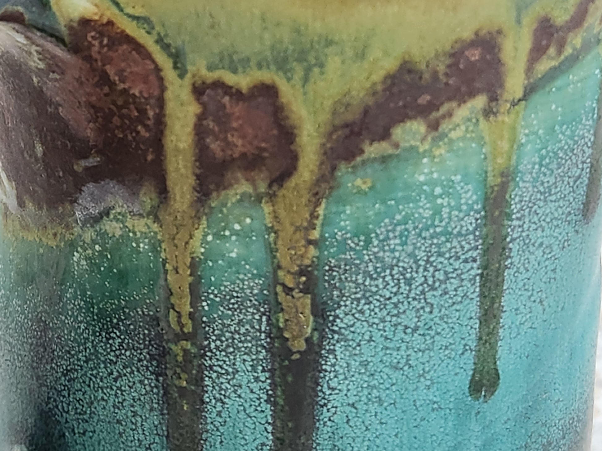 Close-up of flowing turquoise, green and earthy brown reactive glaze on a handmade Bush Creek Earth ceramic mug.