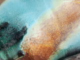 Close-up of handmade pottery mug showing turquoise, terracotta, green and deep earthy glaze movement