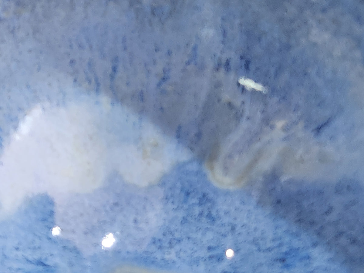 Close-up of a blue ceramic condiment bowl with a rounded rim and an unglazed cream base.