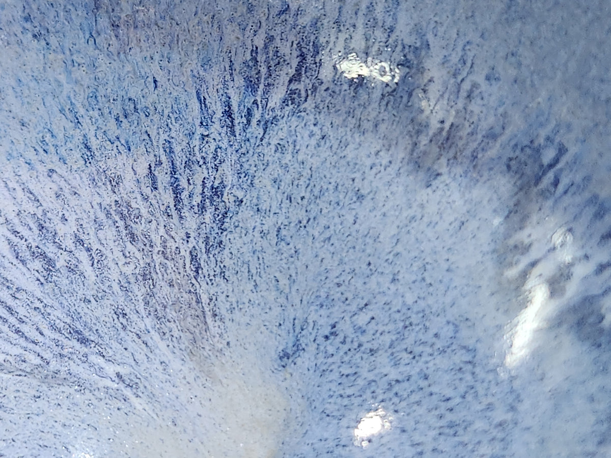 Close-up of delicate blue glaze streaks radiating from the centre of a handmade bowl.