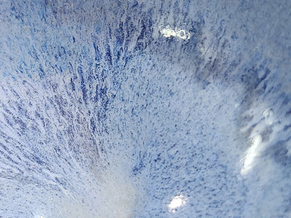 Close-up of delicate blue glaze streaks radiating from the centre of a handmade bowl.