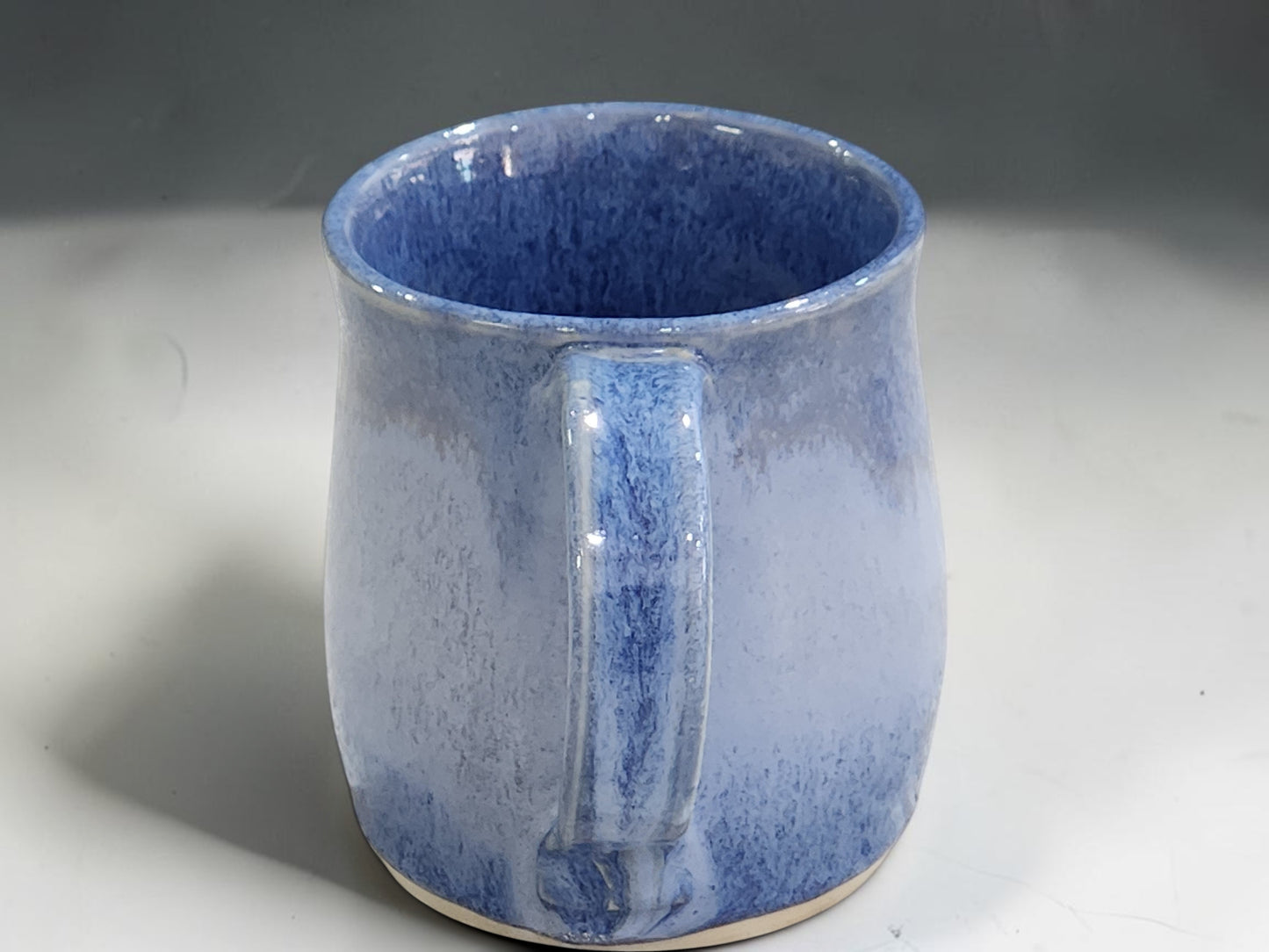 Food-safe handmade pottery mug with flowing blue glaze effects