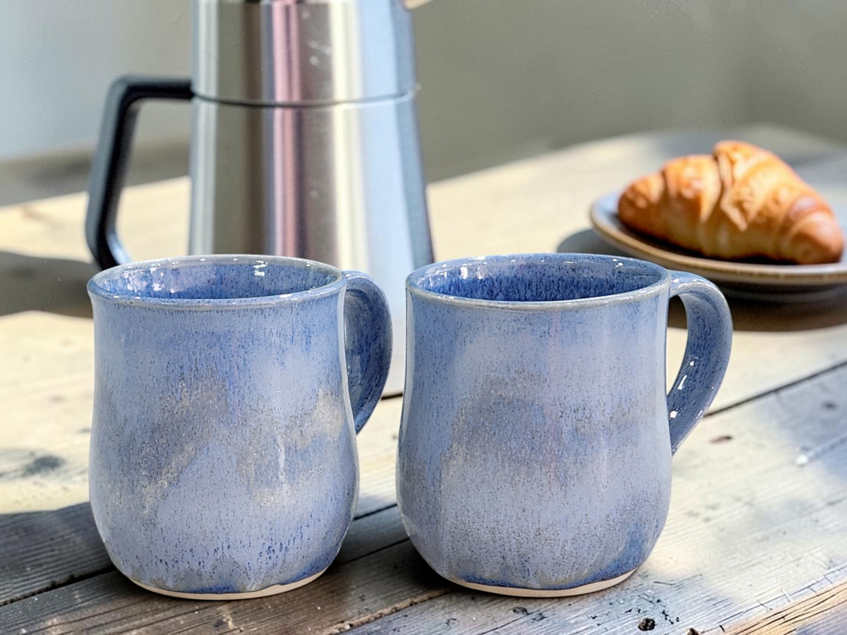 image of two 350ml handmade mottled blue ceramic coffee mugs with French press and croissant