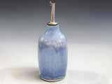 Blue handmade pottery oil bottle with stainless steel pourer in a modern kitchen setting