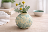 Front view of small moon jar vase with matte crystalline glaze, cream base with teal crystals and glossy green-blue rim