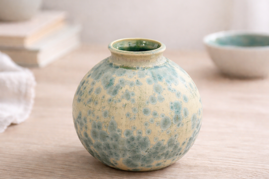 Small handmade pottery vase on bench, moon jar shape with matte cream glaze and teal crystal clusters, Melbourne Australia