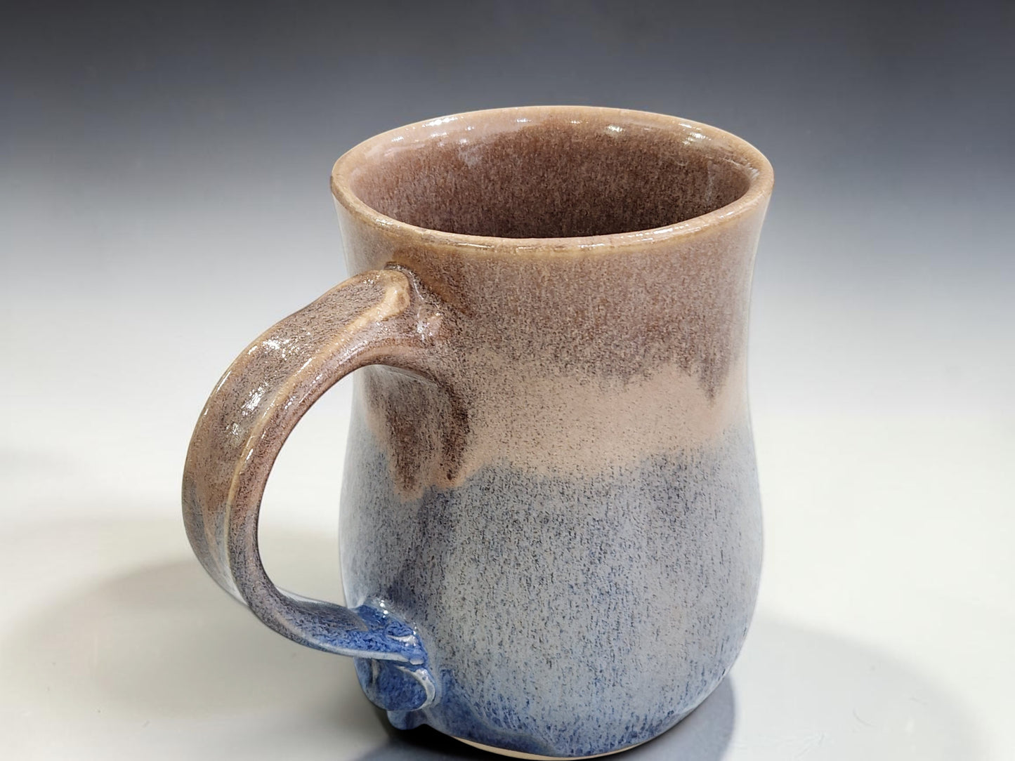 Close-up of handmade ceramic mug with flowing blue and warm oatmeal glaze detail