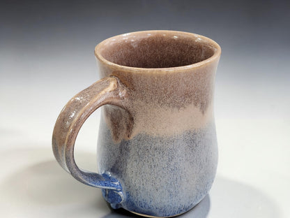 Close-up of handmade ceramic mug with flowing blue and warm oatmeal glaze detail