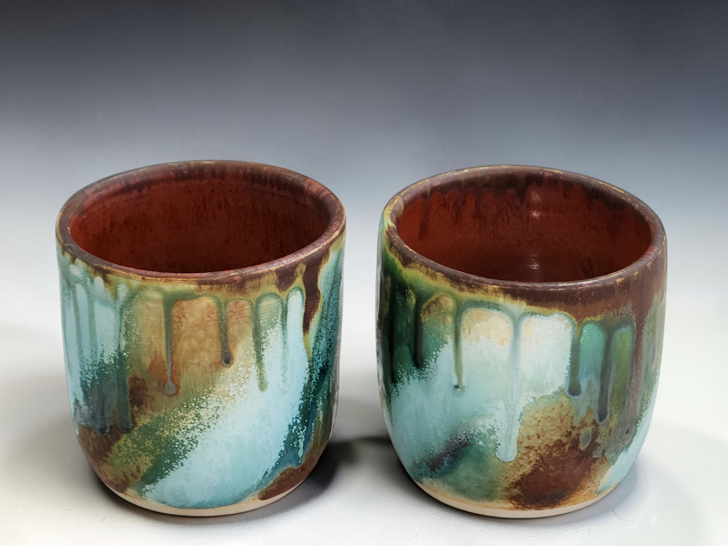 Wheel thrown ceramic tumbler with flowing turquoise, amber and brown glaze
