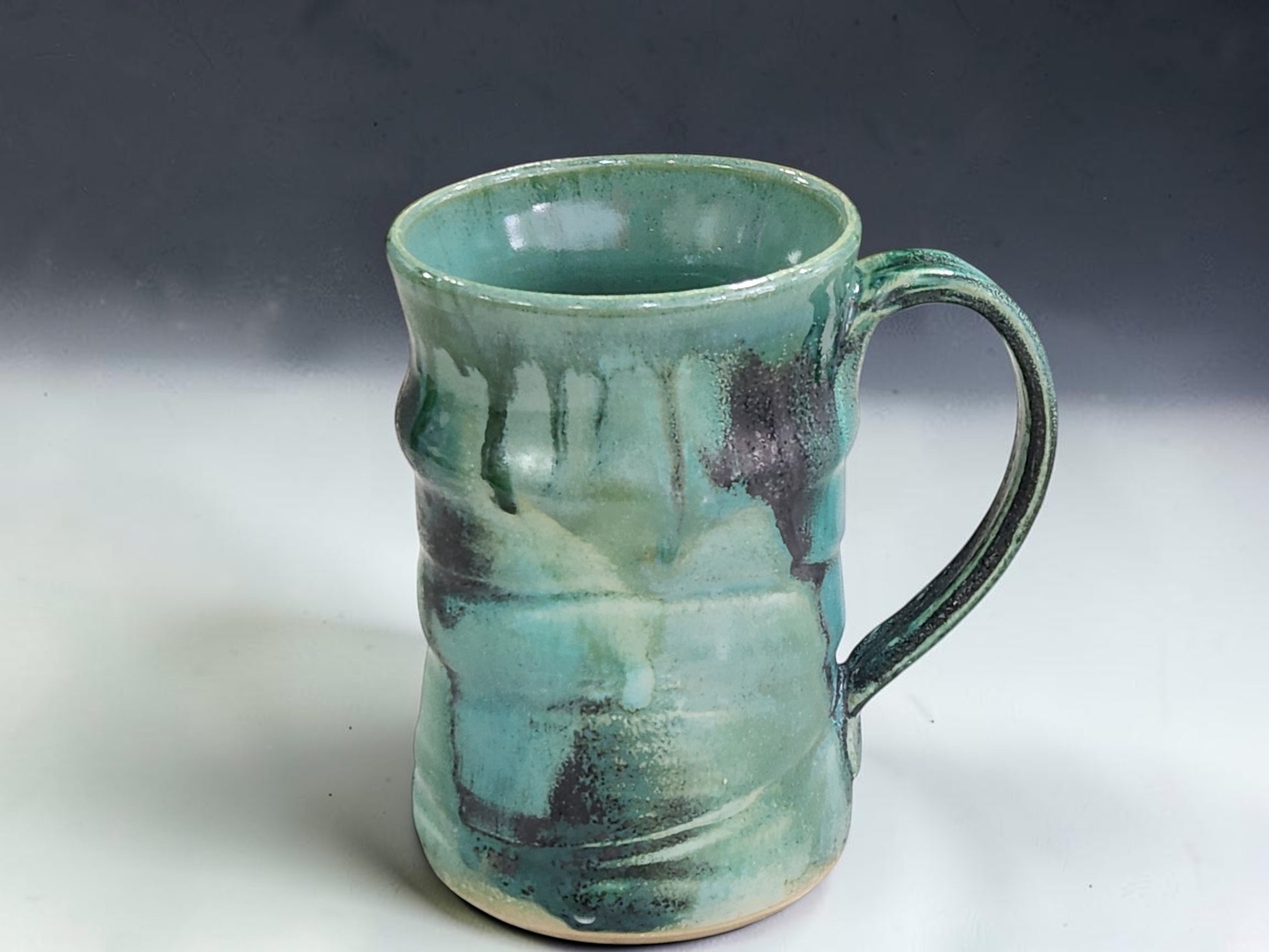 Rustic handmade stoneware mug in blue green and earthy tones, styled in a cosy kitchen coffee scene