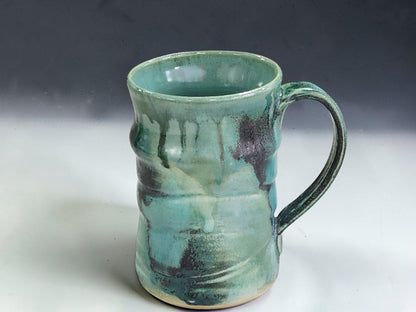Rustic handmade stoneware mug in blue green and earthy tones, styled in a cosy kitchen coffee scene