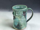 Rustic handmade stoneware mug in blue green and earthy tones, styled in a cosy kitchen coffee scene