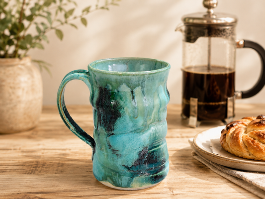Handmade ceramic mug in Bush Creek glaze styled with a French coffee press and pastry in a warm kitchen setting
