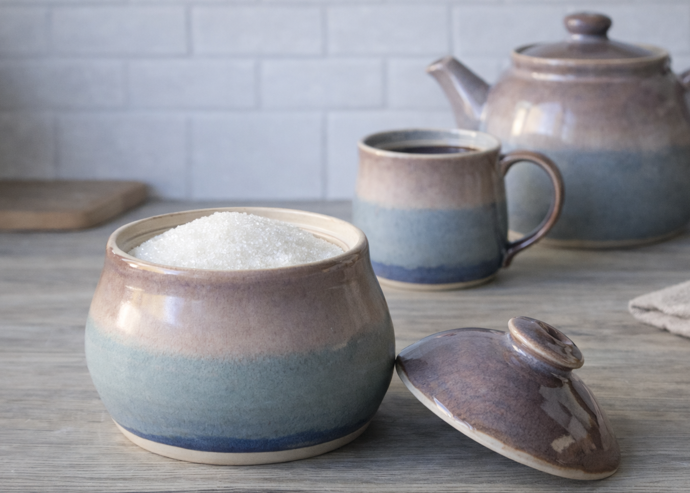 Handmade ceramic sugar bowl with lid in soft blue and beige glaze on kitchen benchtop