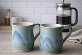 Handmade ceramic mug set in blue and green glaze on kitchen bench with coffee pot”