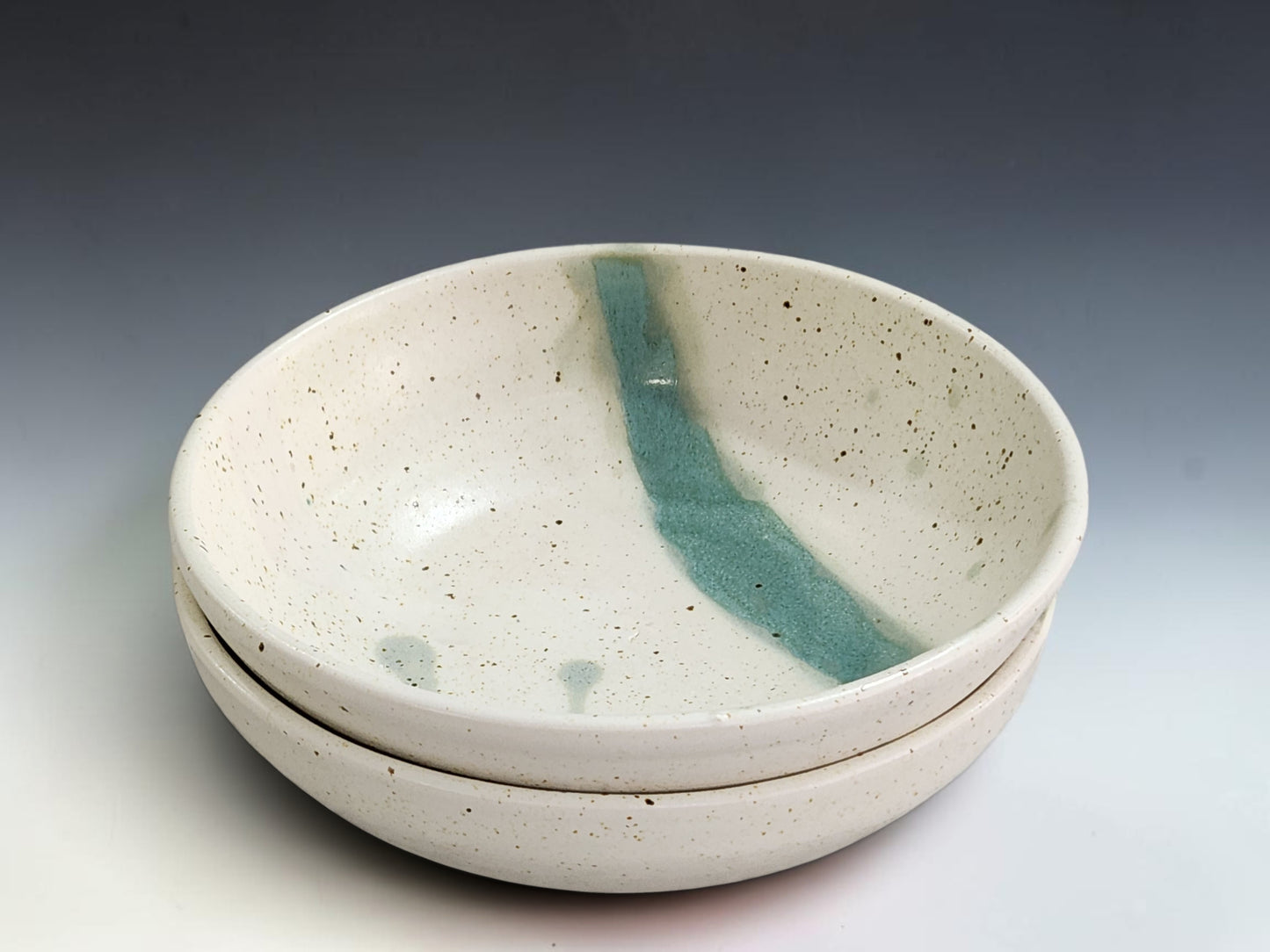 Handmade pottery pasta bowl with soft cream speckled glaze and green interior accent