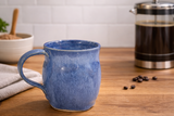 Blue handmade pottery mug on timber benchtop with French press in lifestyle setting