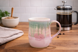 Pink and green handmade pottery mug on timber benchtop in lifestyle kitchen setting