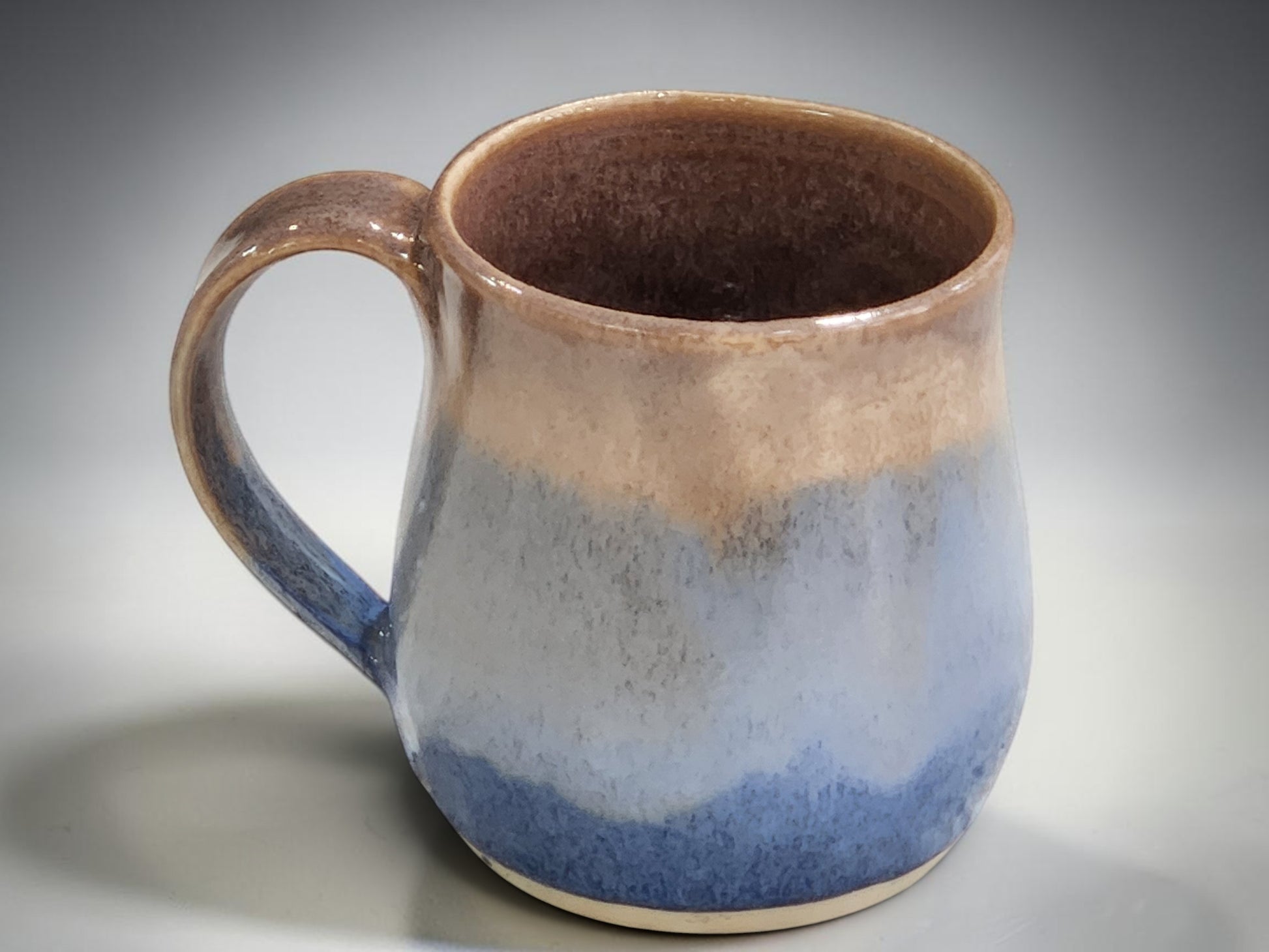 Handmade ceramic mug with flowing blue glaze and comfortable handle