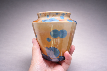 A hand holding a handmade pottery vase with amber glaze and striking blue crystalline details