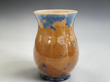 A home decor vase with blue crystals on an amber background.
