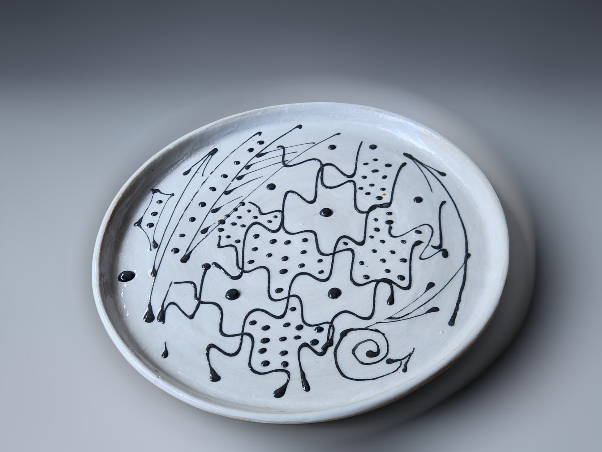 An abstract black slip design on a white pottery plate handmade in Australia.