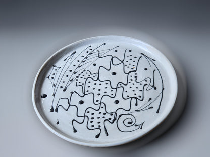An abstract black slip design on a white pottery plate handmade in Australia.