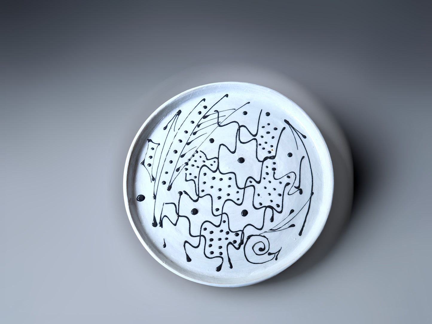 top view of a handmade pottery plate made with a white slip and black decoration.