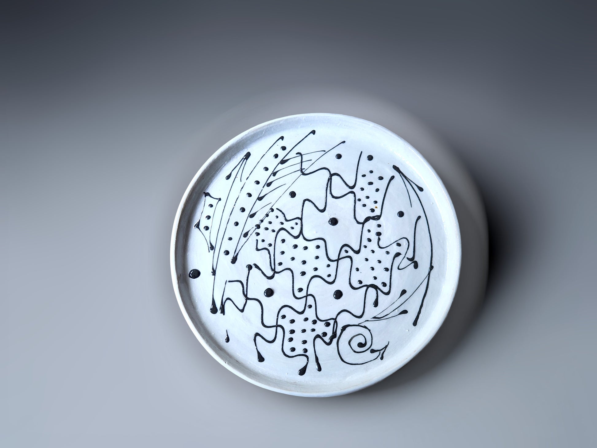 top view of a handmade pottery plate made with a white slip and black decoration.