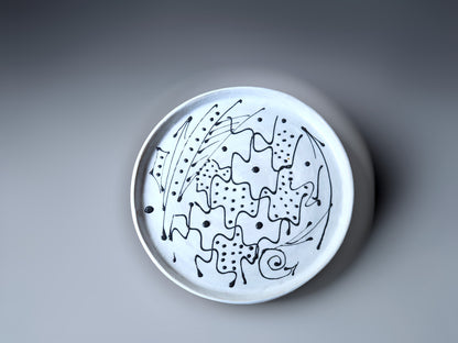 top view of a handmade pottery plate made with a white slip and black decoration.