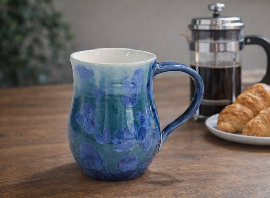 Handmade blue crystalline glaze ceramic mug styled with French press coffee pot and croissants