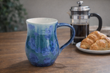 Handmade blue crystalline glaze ceramic mug styled with French press coffee pot and croissants