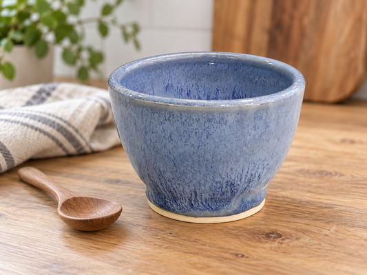 Small blue pottery bowl on a timber benchtop beside a wooden spoon and striped linen.