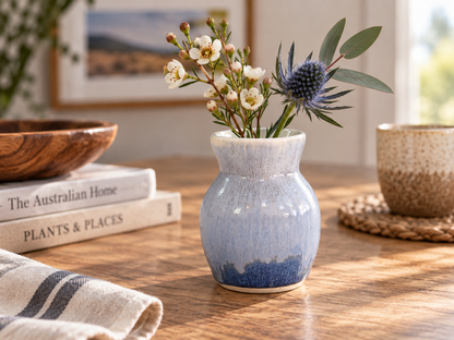 Small handmade blue bud vase with flowers in a warm lifestyle setting