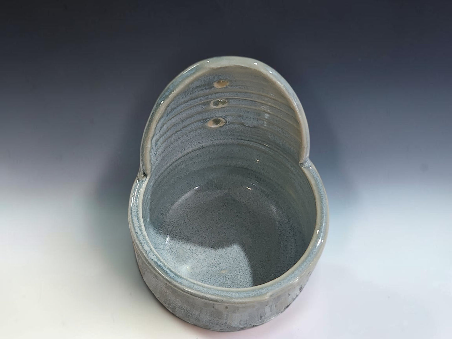 Handmade ceramic herb stripper on grey studio background showing soft blue-grey glaze and stripping holes