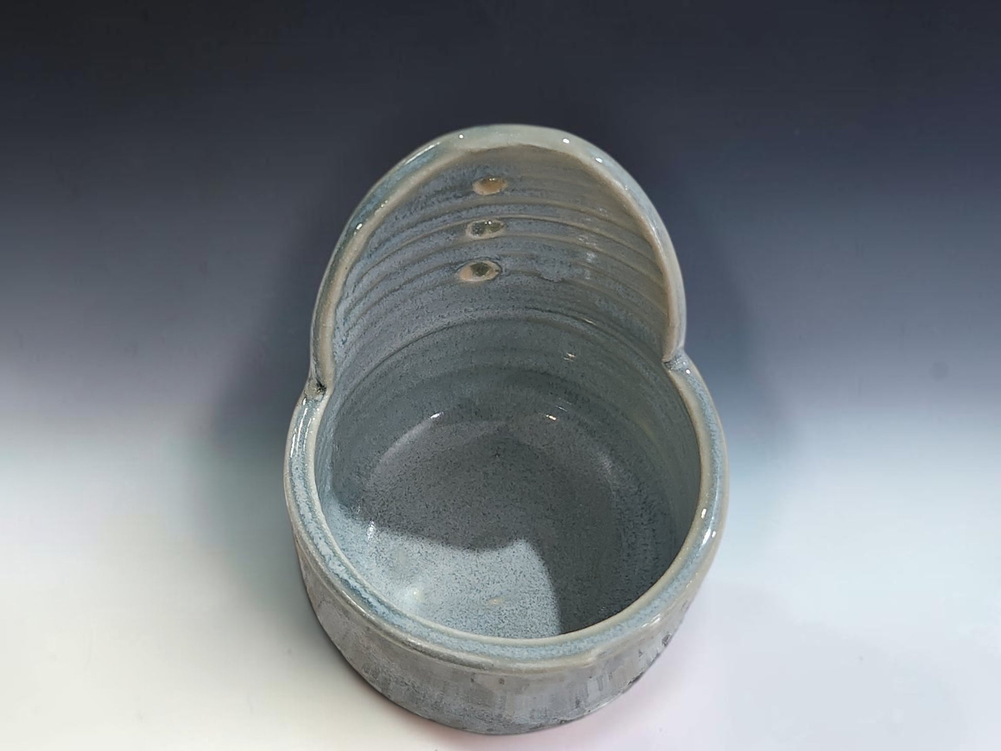 Handmade ceramic herb stripper on grey studio background showing soft blue-grey glaze and stripping holes