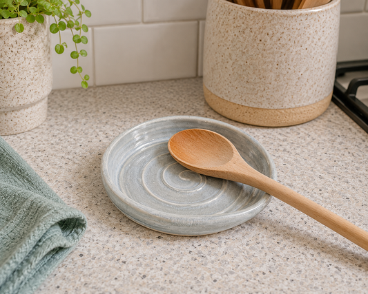 Handmade ceramic spoon rest in soft grey blue glaze styled in a kitchen with a wooden spoon
