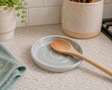 Handmade ceramic spoon rest in soft grey blue glaze styled in a kitchen with a wooden spoon