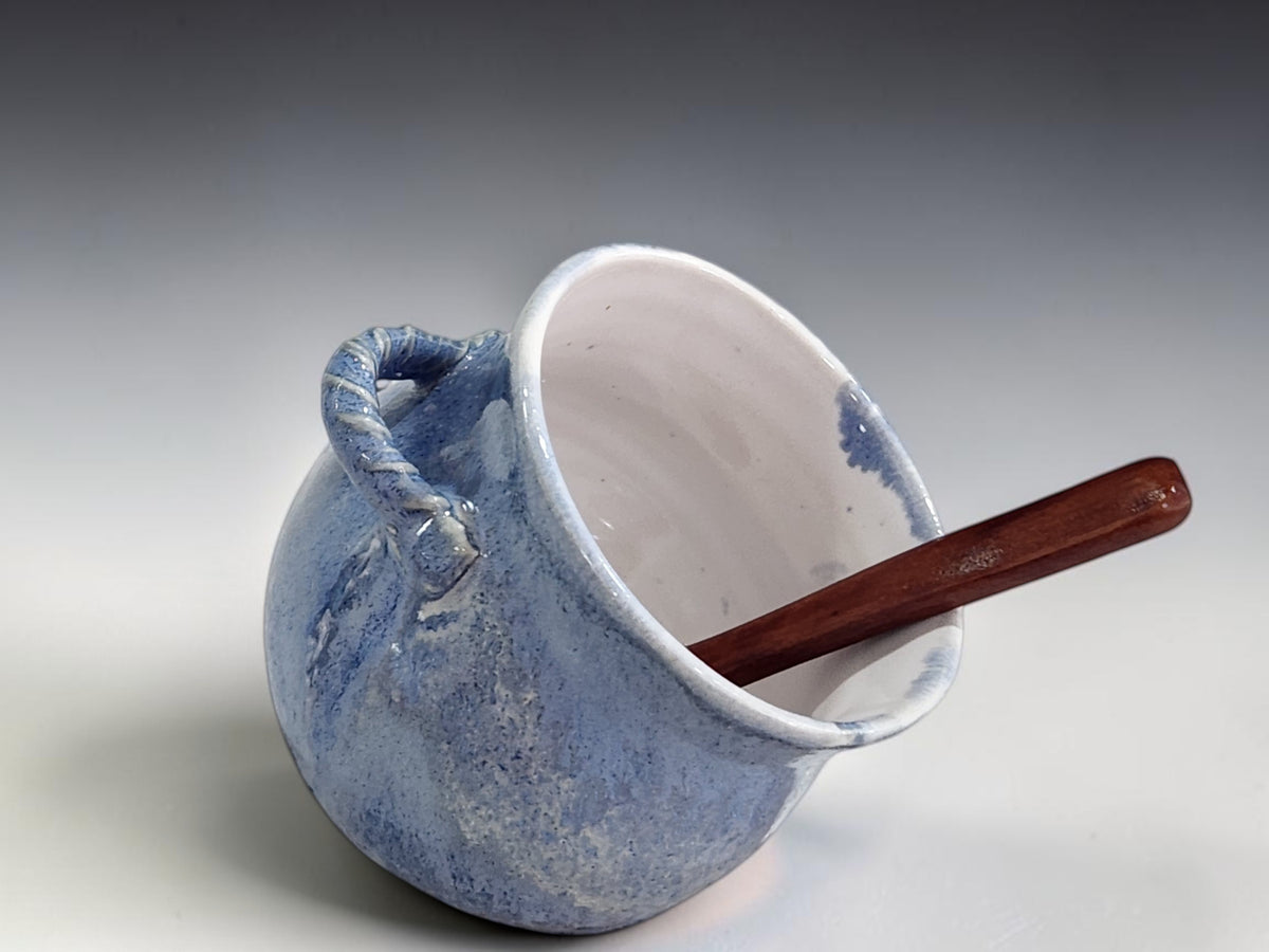 Side view of rounded blue pottery salt pig with wooden spoon