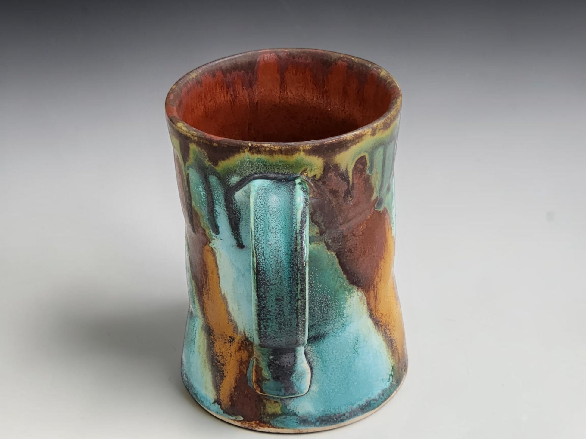 Side view of a handmade stoneware mug showing organic glaze movement in turquoise, green and warm terracotta tones.