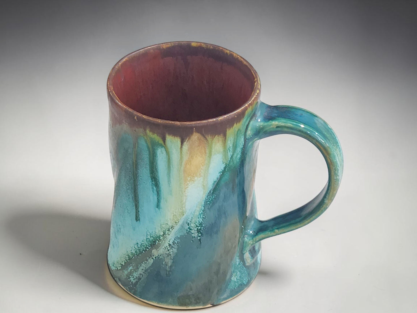 Studio view of handmade ceramic coffee mug with tall wheel-thrown form and ergonomic handle