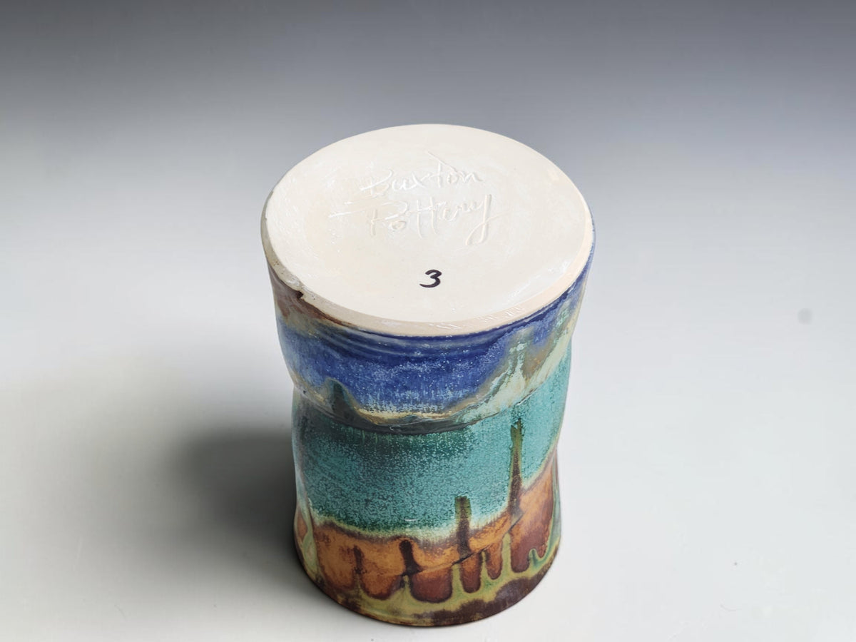 Underside of a Bush Creek coffee mug with long green glaze trails and blue accents near the base.