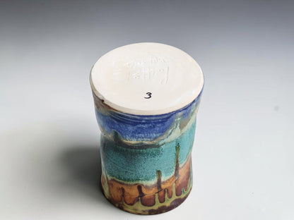 Underside of a Bush Creek coffee mug with long green glaze trails and blue accents near the base.