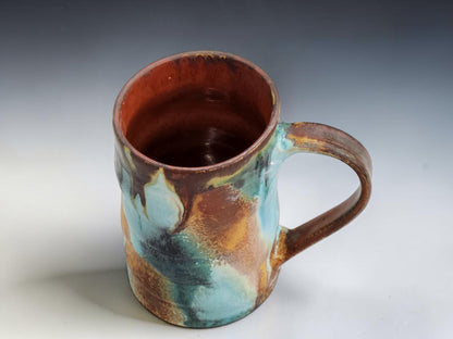 Wheel-thrown pottery mug with altered shape and organic glaze movement on a grey gradient studio background
