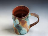 Wheel-thrown pottery mug with altered shape and organic glaze movement on a grey gradient studio background