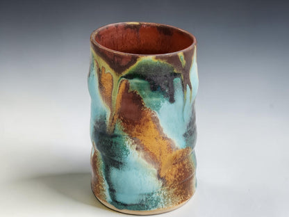 Handmade ceramic coffee mug in turquoise, rust brown and moss green glaze, photographed on a neutral grey studio sweep
