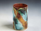 Handmade ceramic coffee mug in turquoise, rust brown and moss green glaze, photographed on a neutral grey studio sweep
