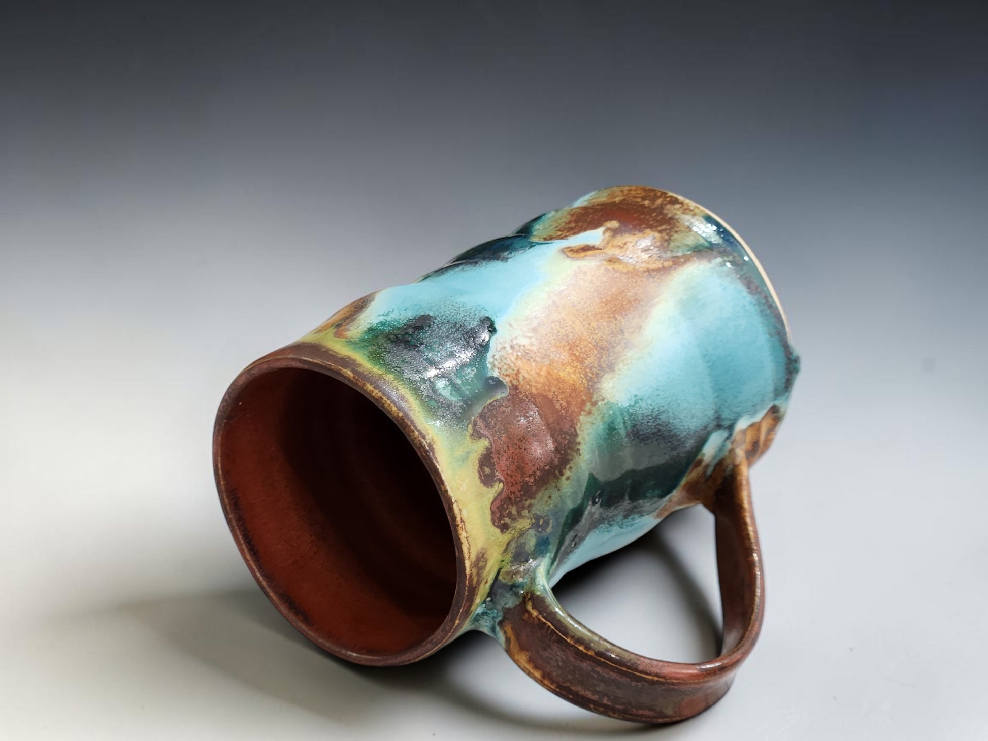 Handmade ceramic mug with curved handle, glossy layered glaze and natural handmade variation on grey background