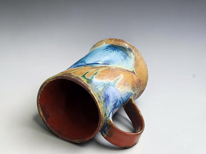 Handmade pottery mug with blue, green and brown mingled glazes .