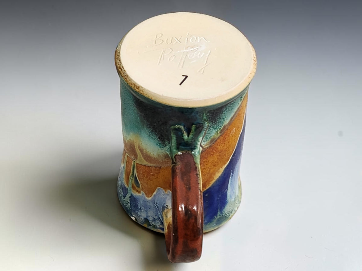 Close-up underside  of layered blue, cream, green and ochre glaze on a handmade pottery mug.